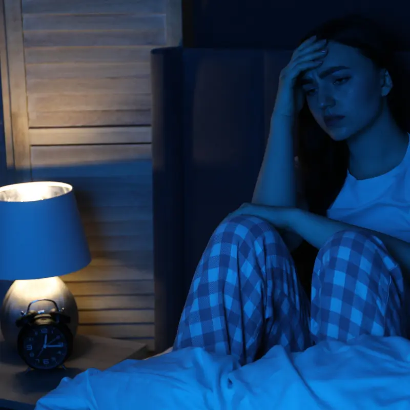 alteracion_del_sueño Mujer sentada en la cama con la cabeza apoyada en el brazo, con la luz de la mesita de noche y sin poder dormir